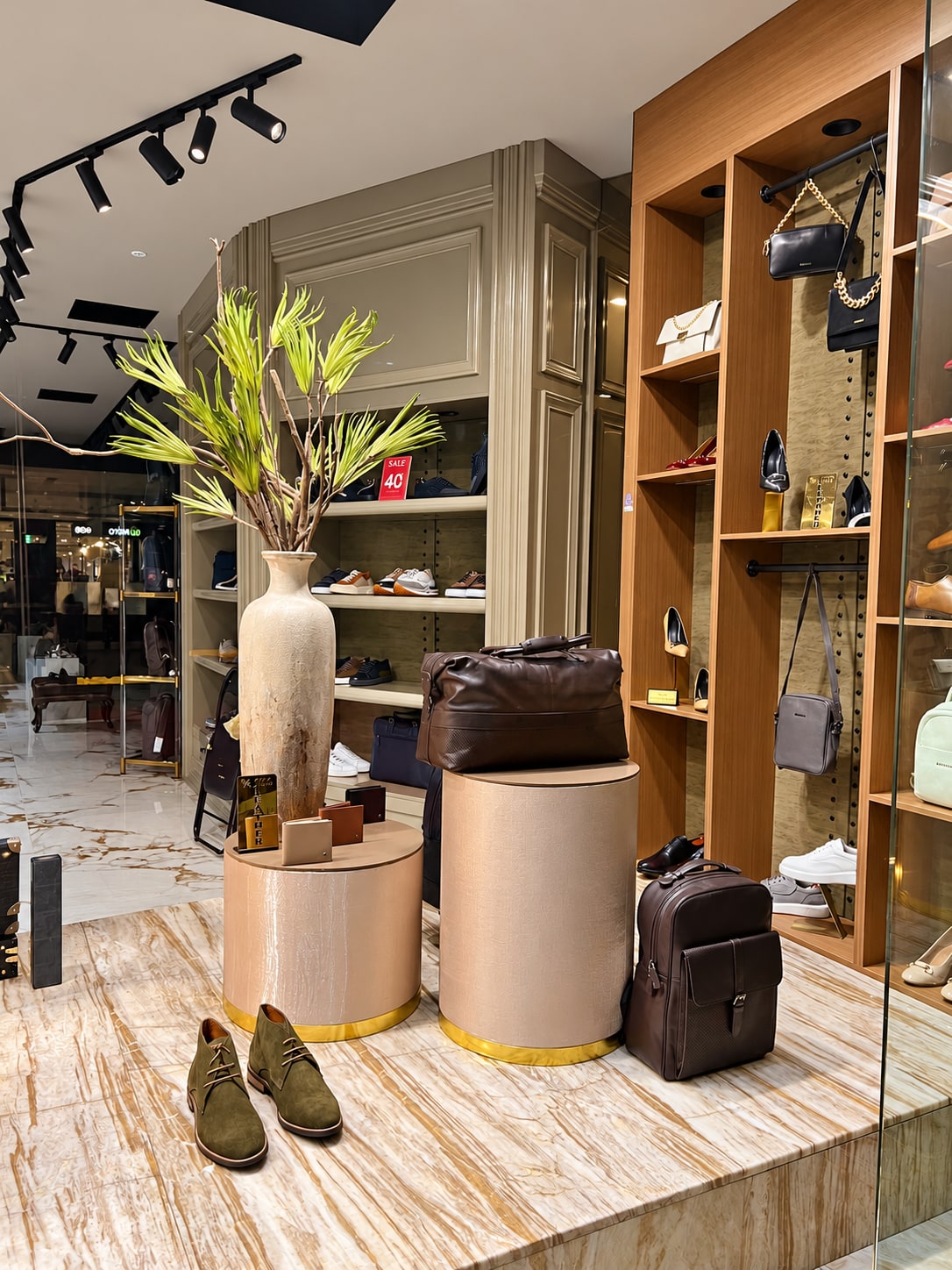 Leather bags, wallets and shoes styled on gold-trimmed plinths beside a tall vase